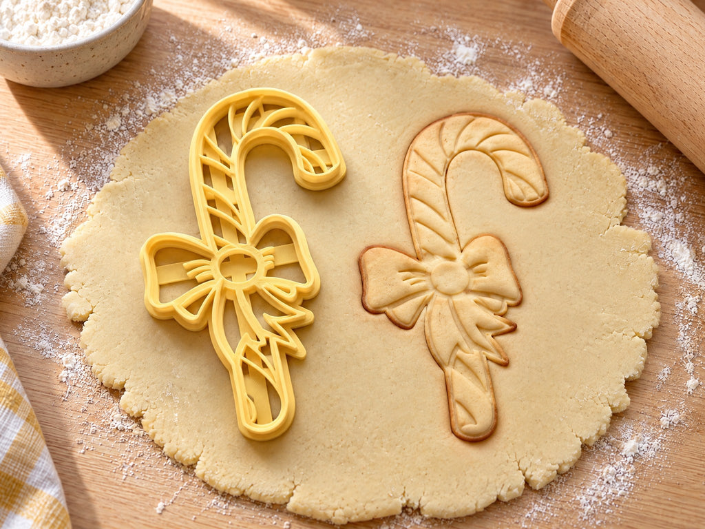 Butter-gelber Zuckerstangen-Ausstecher mit Prägung neben gebackenem Keks mit Ringeln und flatternder Schleife auf hellem Holz